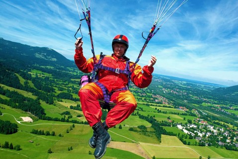 A paraglider in orange and red overall flies over the meadows at Brauneck near Lenggries, Bavaria,