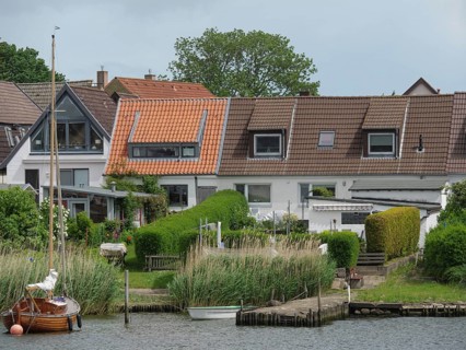 Terraced houses with well-kept gardens and boats along a riverbank in a quiet residential area,