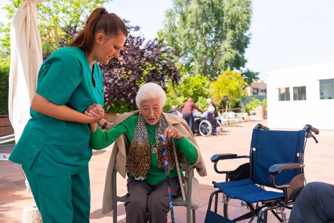 An elderly woman with the nurse in the wheelchair in the garden of a nursing home or retirement