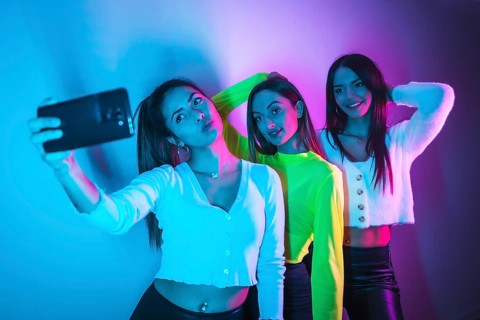 Lifestyle of friends partying in a nightclub with blue and pink neon lights, taking a selfie with
