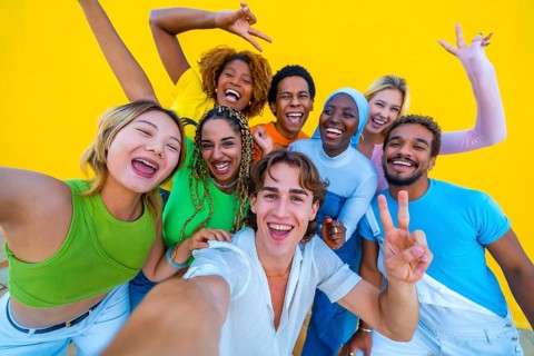 Young people from different ethnicities taking a happy selfie at a gathering next to a yellow