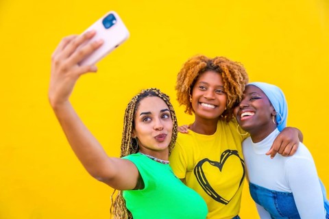 Portrait with copy space of three female friends taking a selfie together in a yellow background