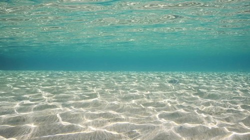 Sandy shallow water in sunburst and glare on seabed sand. Sunlight passes through surface of
