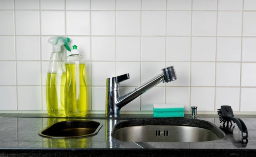 kitchen sink and faucet with a sponge and brush on a black granite table top and yellow kitchen
