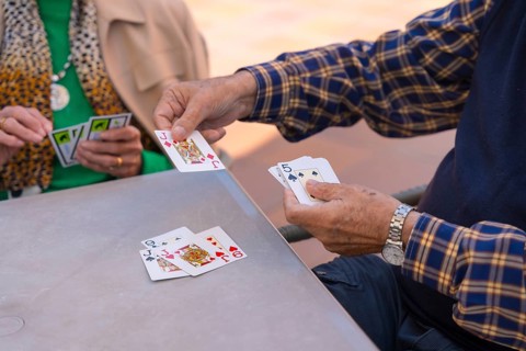 Hands of two elderly people in the garden of a nursing home or retirement home playing cards on a