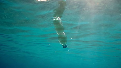 Green plastic bottle drifting under surface of blue water. Plastic pollution of Ocean, Discarded