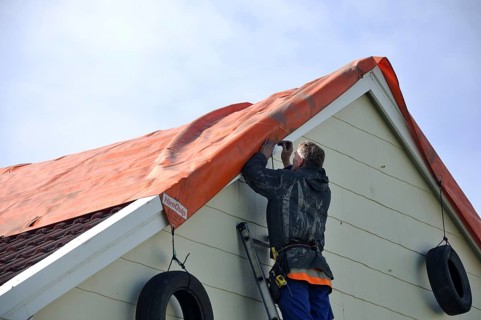 GREYMOUTH, NEW ZEALAND, APRIL 17, 2014: Volunteer worker places a tarpaulin on a house de-roofed in