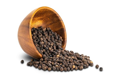 Closeup view pile of dried natural black pepper seeds in wooden cup on white background with