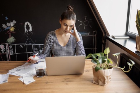 Serious housewife sits at table at home kitchen check household bills, make calculations on