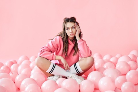 Bored fashionable woman sitting on floor with pink air balloons on pink pastel background.