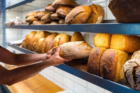 Hands of baker employee of bakery in workshop workshop of artisan bakery placing baked bread from