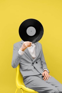 Man covering his face with vinyl record while wearing ultimate gray clothes. High resolution photo