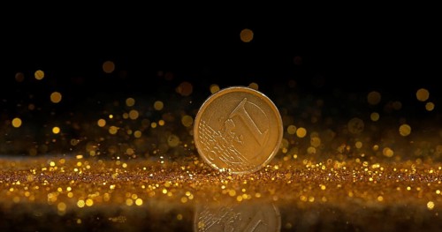 Coin of 1 Euro Rolling on Gold Powder against Black Background