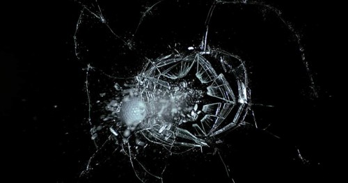 Golf Ball breaking Pane of Glass against Black Background