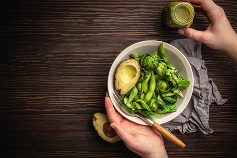 Bowl of healthy salad in female hands from above and green detox smoothie in a bottle on wooden