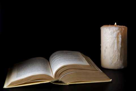 Open book illuminated by candlelight isolated on a black background