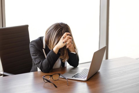 Young female manager taked of glasses after typing on netbook keyboard while sitting at table and