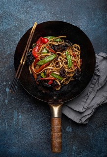 Asian dish stir fry udon noodles with vegetables and mushrooms in black rustic wok pan with wooden