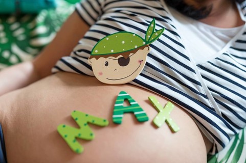 A wooden replica of a baby boy's face and letters for the name Max lie on a pregnant woman's belly