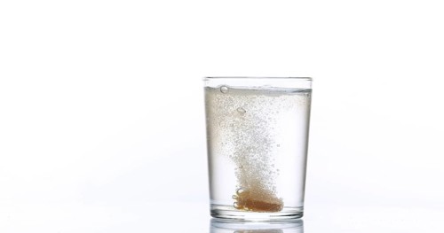 Tablets Falling and Dissolving into a Glass of Water against White Background