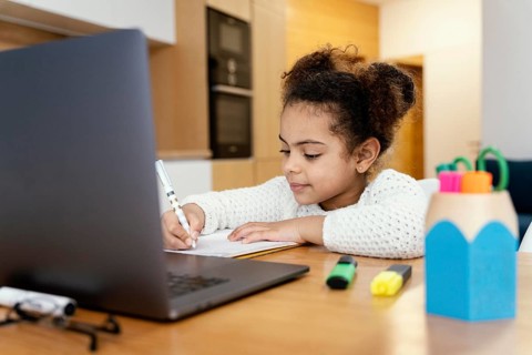 Little girl home studying during online school with laptop