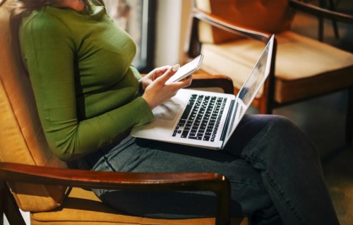Side view of happy woman smiling and browsing laptop while sitting at table and working on remote