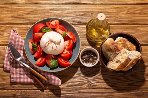 Italian salad with fresh tomatoes, burrata cheese, basil served on ceramic plate with ciabatta