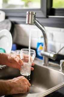 Man pouring water into glass in kitchen, closeup