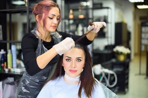 Professional female hairdresser applying color to female customer at design hair salon, woman