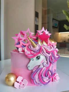 A whimsical unicorn birthday cake with pink and gold decorations, featuring pastel flowers and star