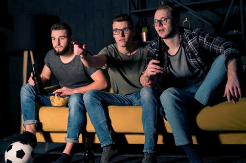 Front view male friends watching sports tv together while having snacks beer