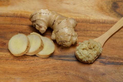 Ground ginger in a wooden spoon with fresh ginger root cut in slices