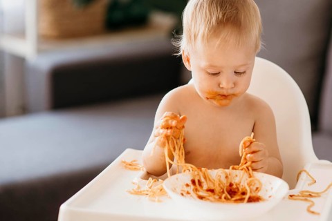 Baby boy eating pasta his highchair making mess
