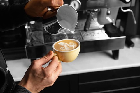 Close up hand pouring milk delicious coffee cup