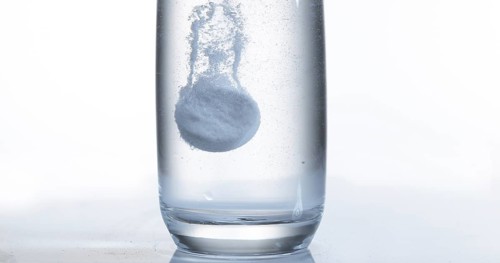 Tablets Falling and Dissolving into a Glass of Water against White Background