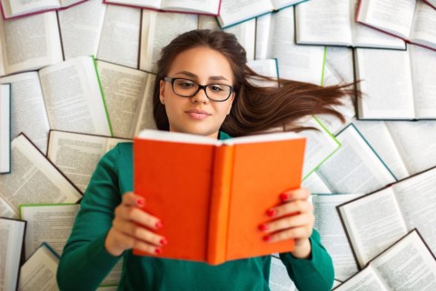 Top view of female student lying on books and reading during exam preparation