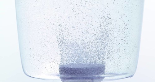 Tablets Falling and Dissolving into a Glass of Water against White Background