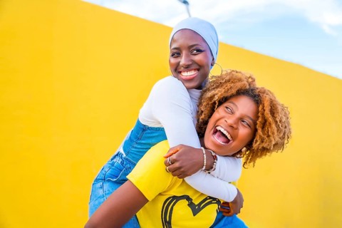 Happy scene of a muslim woman piggybacking an african friend outdoors