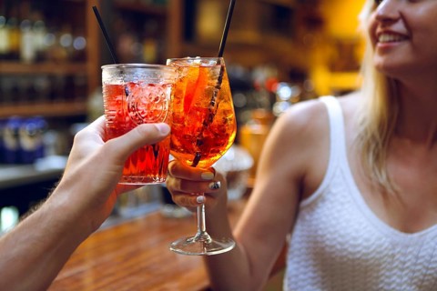 Woman and man raising a glasses of coktails in the bar background