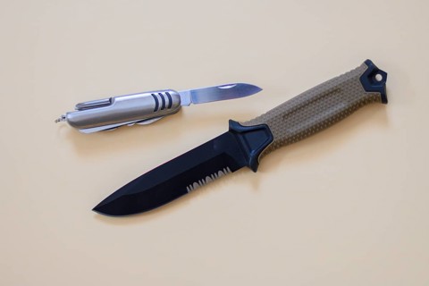 A hunting knife with a beige handle lies next to a Swiss Army knife on a cream-coloured surface