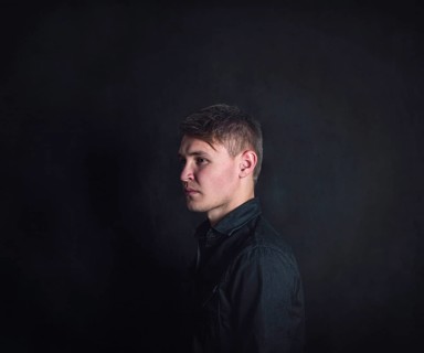 Thoughtful young man side view portrait, looks upset and tired against a dark wall background.