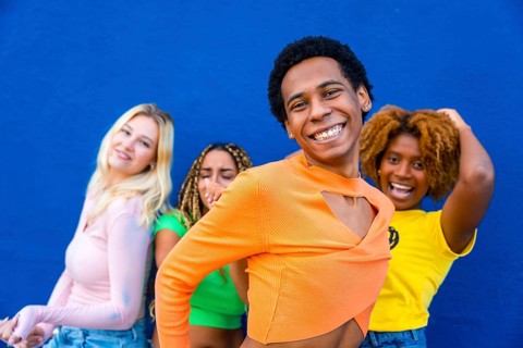 Close-up of a transgender person dancing happily with multi-ethnic friends next to a blue wall