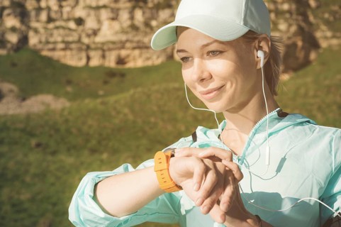 Portrait of a smiling young fitness girl in a cap and headphones checking her smart clock while