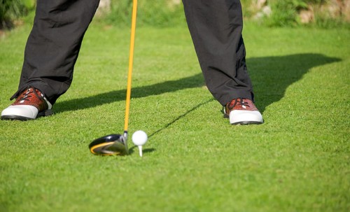 Golfer addresses golf ball with driver in tee box
