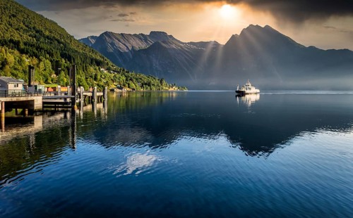Ferry arriving on fjord during sunrise in norway with mountains in background