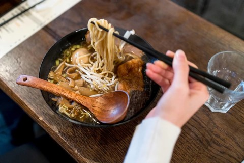 Woman using chopsticks to eat a ramen soup served on a bowl in a restaurant