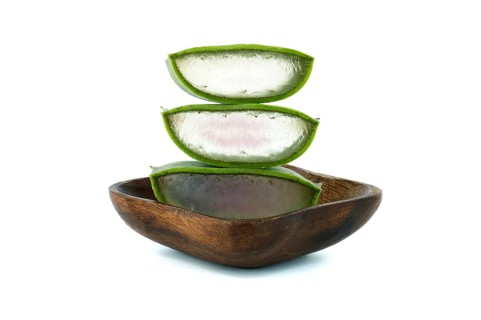 Aloe Vera leaf slices in wooden plate isolated on white background, organic cosmetic ingredients,