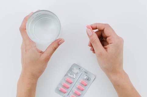 Close up woman s hand holding pink pills glass water white background