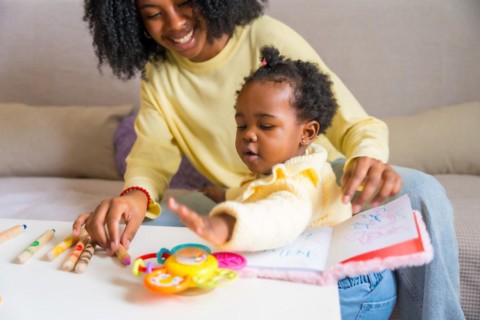 Little cute african daughter and mother playing in the sofa with toys and books