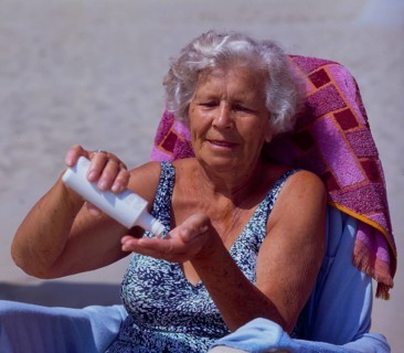 Old woman with sun cream on the sandy beach
